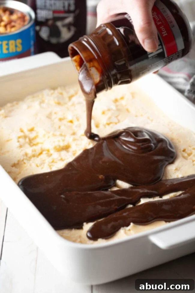 Gently pouring warm hot fudge sauce over the creamy vanilla ice cream layer, preparing for the next delicious step.
