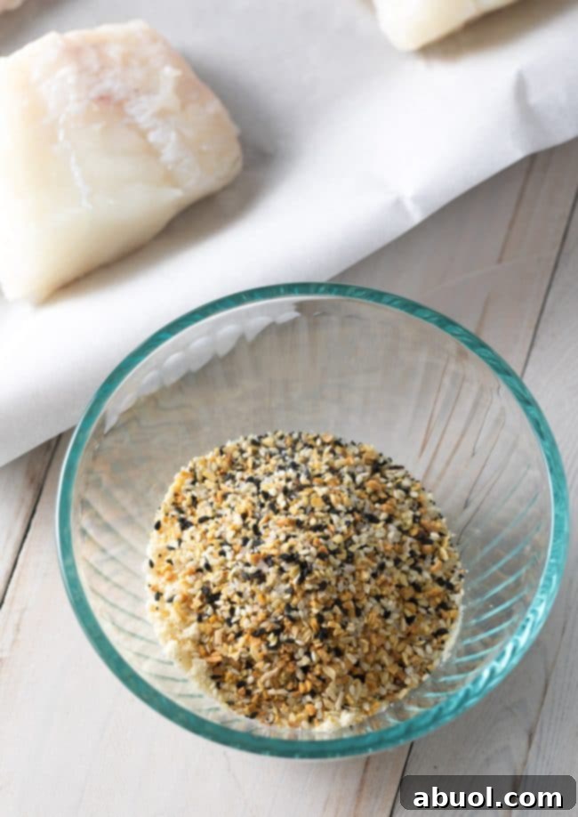 Fresh raw white fish fillets placed next to a small bowl brimming with everything bagel seasoning, ready for preparation.