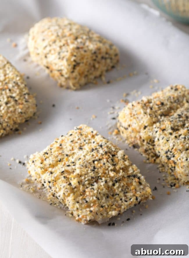 Raw white fish fillets laid out on a baking dish, each evenly coated with a vibrant everything bagel seasoning crust, ready for the oven.