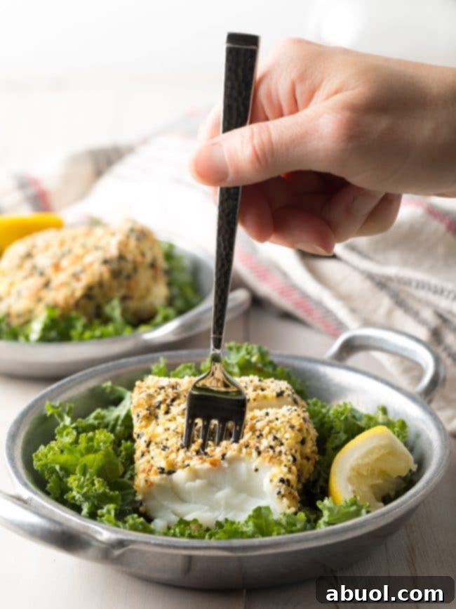 A hand gently flaking a piece of perfectly cooked cod with a fork, revealing its moist and tender interior.