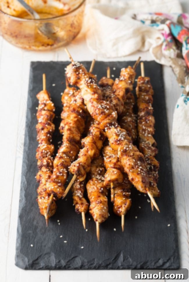 A plate of finished Korean chicken skewers, garnished with sesame seeds and green onions.