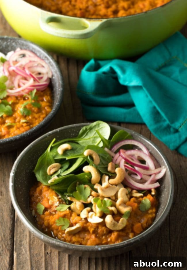 Bowl of curry with fresh baby spinach, all topped with whole raw cashews, red onion slices, and chopped fresh cilantro.