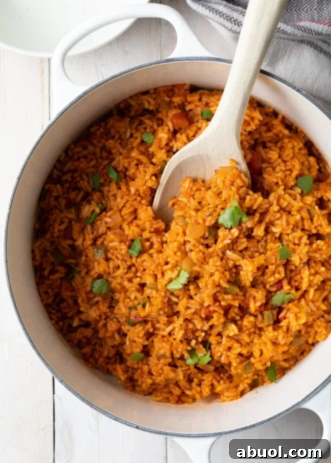 A Dutch oven filled with freshly cooked Spanish rice, ready to be served, with a wooden spoon resting in it.