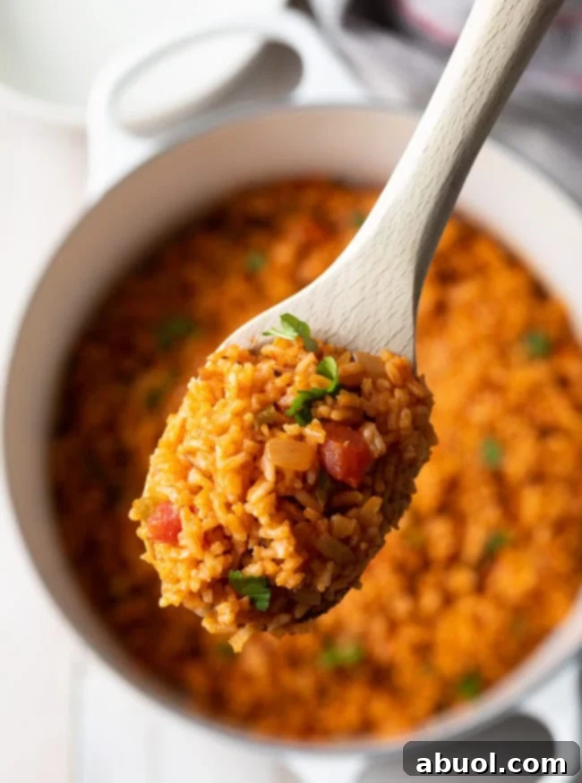 A wooden spoon lifting a scoop of fluffy Spanish rice from a pot, showcasing its vibrant color and texture.