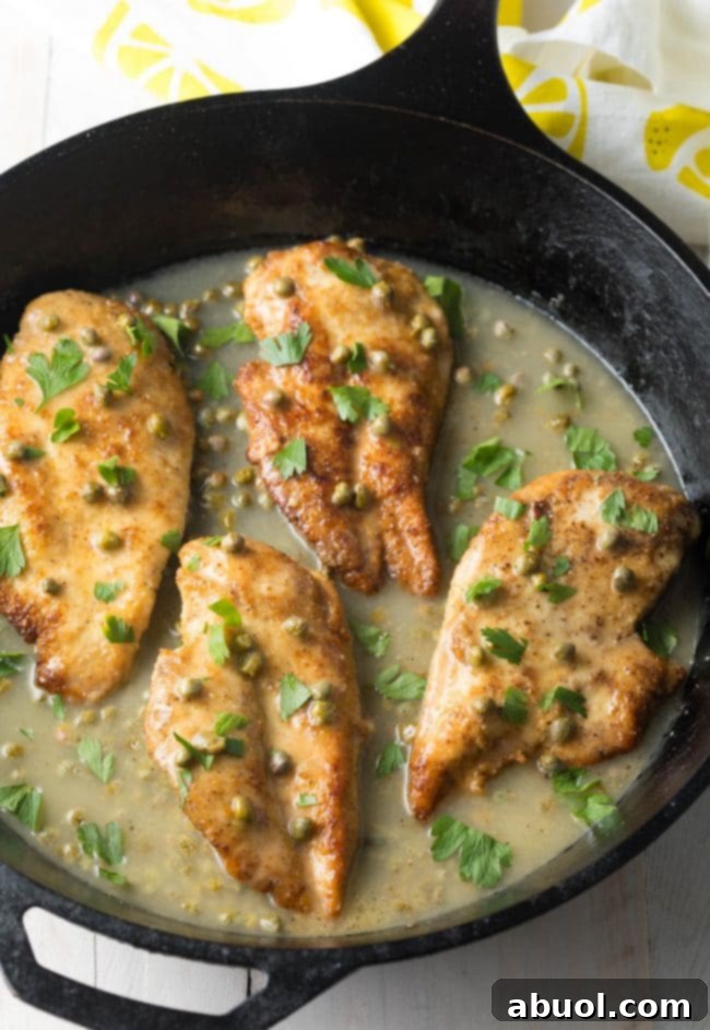 Best chicken piccata recipe overhead shot in cast iron skillet, garnished with fresh parsley and lemon slices.