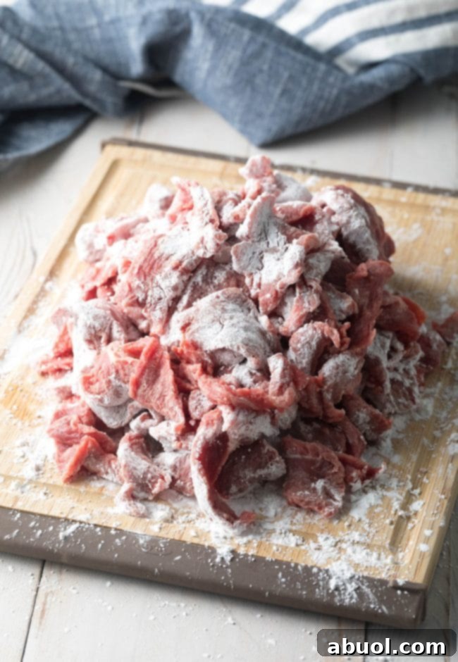 Finely sliced Szechuan beef pieces lightly coated in flour, ready for stir-frying in a hot wok to achieve perfect crispiness.