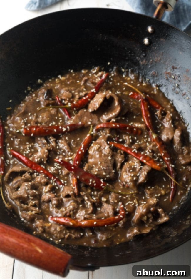Szechuan beef stir-frying in a pan with colorful peppers and a rich sauce, creating an aromatic and visually appealing dish.