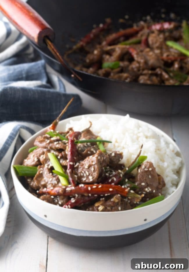 A bowl of freshly prepared Szechuan Beef, perfectly coated in sauce and served with a side of white rice, garnished with scallions.