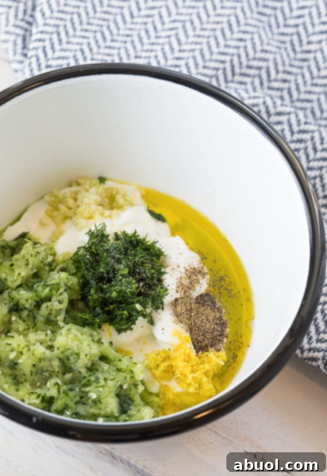 A bowl filled with fresh ingredients for Tzatziki sauce, including creamy Greek yogurt, shredded cucumber, fresh dill, lemon, and garlic cloves, ready to be mixed.