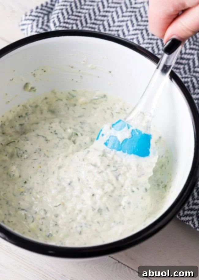 A medium bowl containing freshly mixed ingredients for Tzatziki, showcasing the creamy texture with flecks of cucumber and dill throughout.