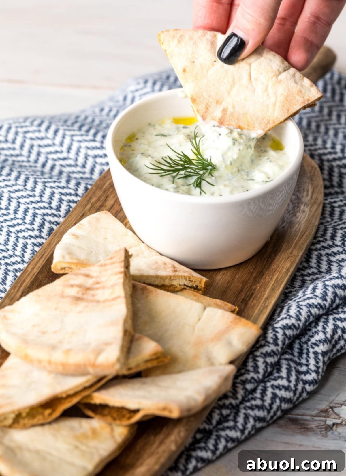 A hand gracefully dipping a piece of fluffy pita bread into a bowl of perfectly prepared homemade Tzatziki sauce, highlighting its creamy texture.