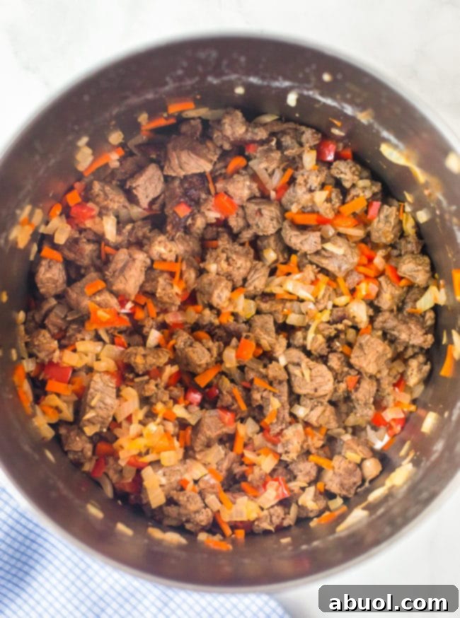 Diced steak and colorful vegetables sautéing in a large stock pot, forming the flavorful base of the chili.