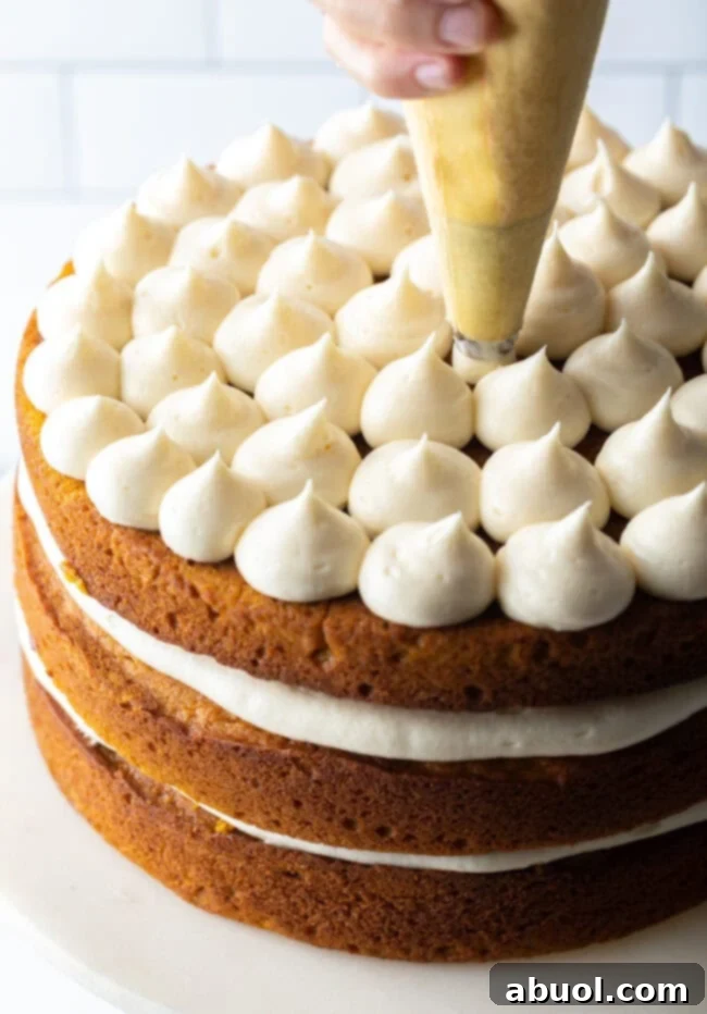 Spiced Autumn Pumpkin Cake 9 Hand piping frosting onto top layer of cake.