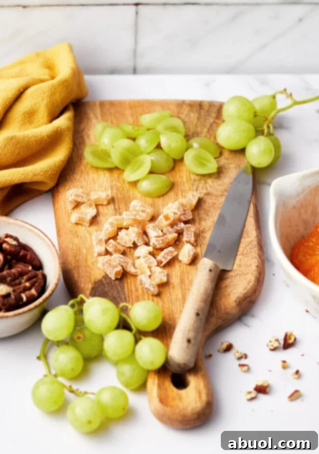 Chopped ingredients for ambrosia fruit salad on a wooden cutting board with a knife. The chopped ingredients here are grapes and dried fruit and pecans. 