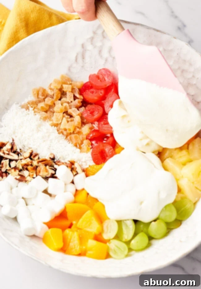 Mixing together canned peaches, maraschino cherries, grapes, pineapple, mini marshmallows, coconut, caramelized ginger, and chopped pecans with cool whip and sour cream.