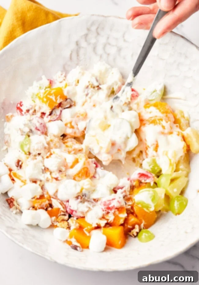 Overhead view of a spoon mixing together the ambrosia salad in a mixing bowl. 