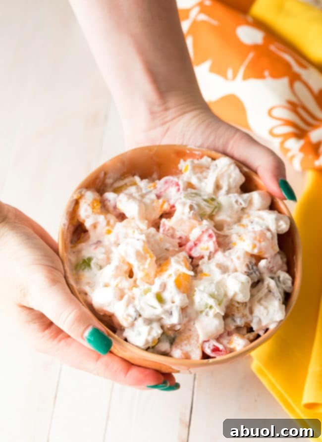 Two hands holding a bowl of fluffy marshmallow and canned fruit salad.