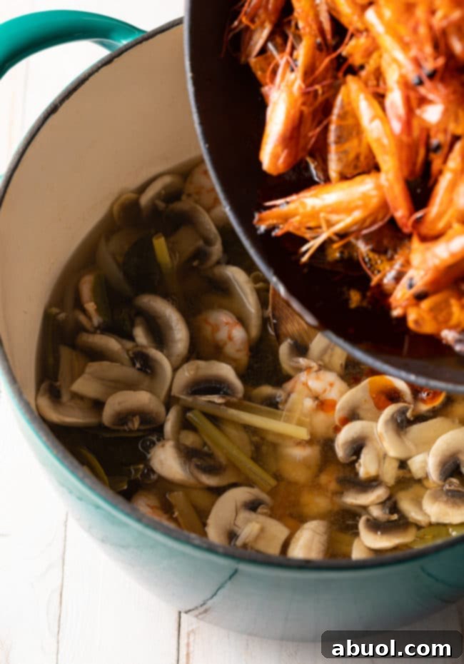 Spicy Thai Tom Yum Perfection 9 Adding cooked shrimp to a soup pot with mushrooms and lemongrass.