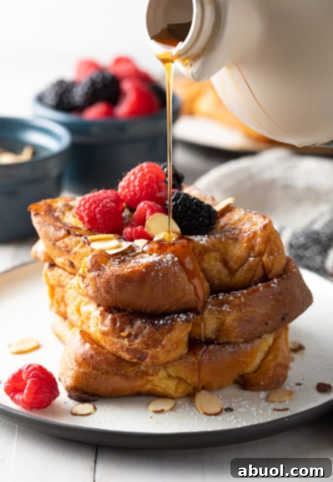How To Make Pain Perdu - golden French toast piled high on a white plate, dusted with powdered sugar.