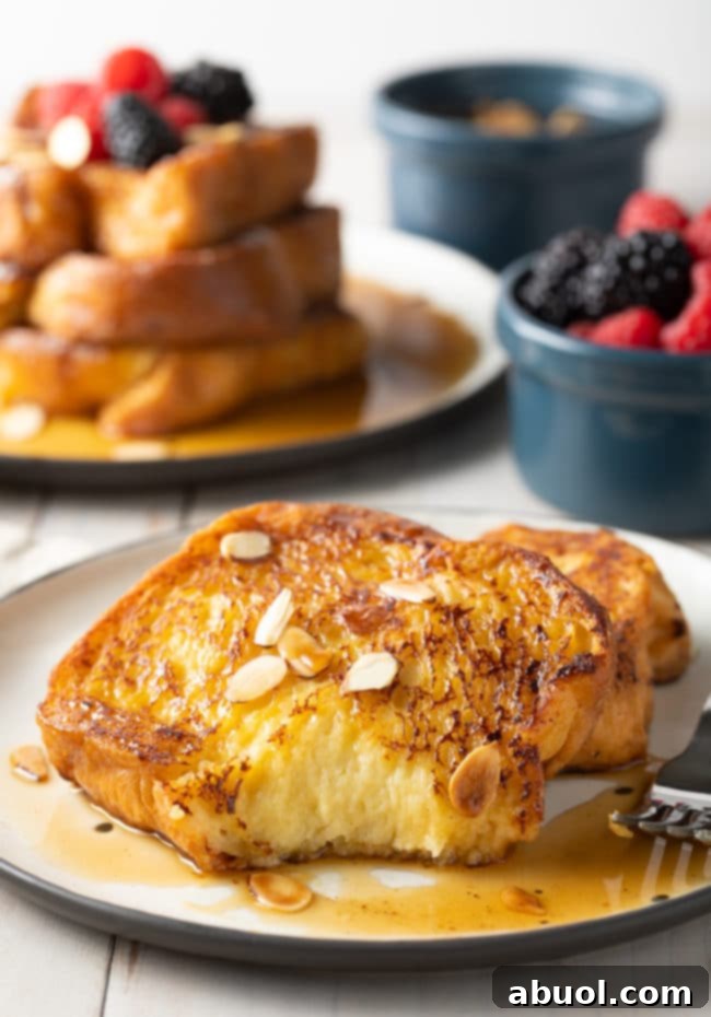 A close-up shot of two slices of Pain Perdu on a white plate, one with a bite taken out, revealing its soft, custardy interior.
