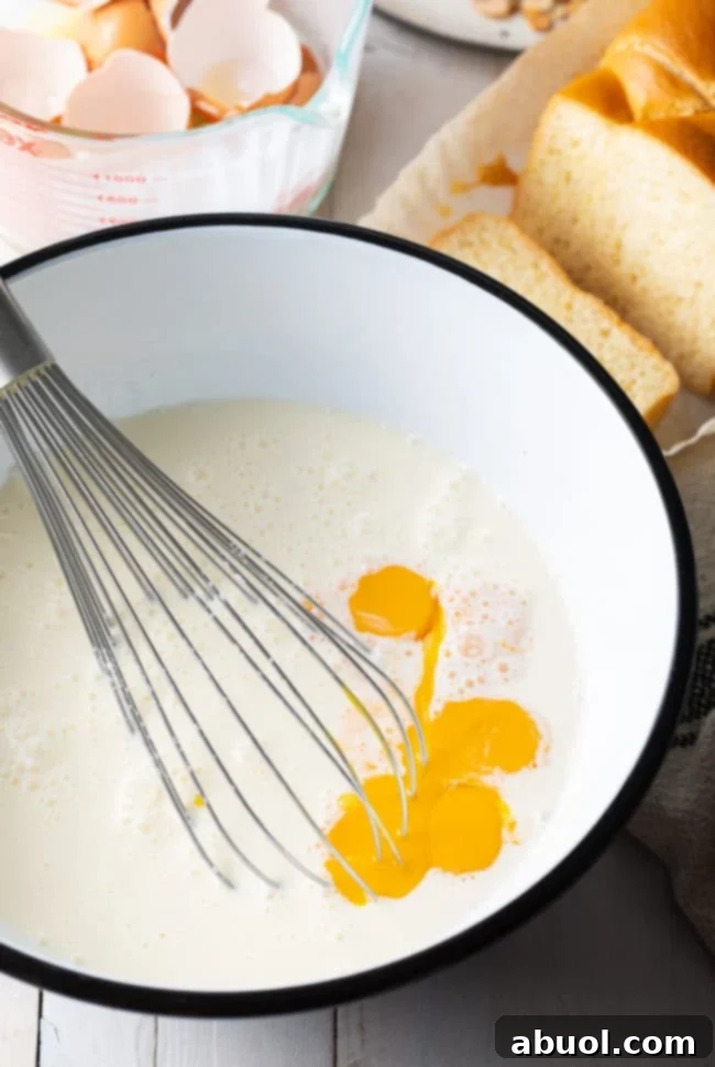 Close-up of a perfectly whisked, creamy egg custard mixture in a white bowl with a whisk.