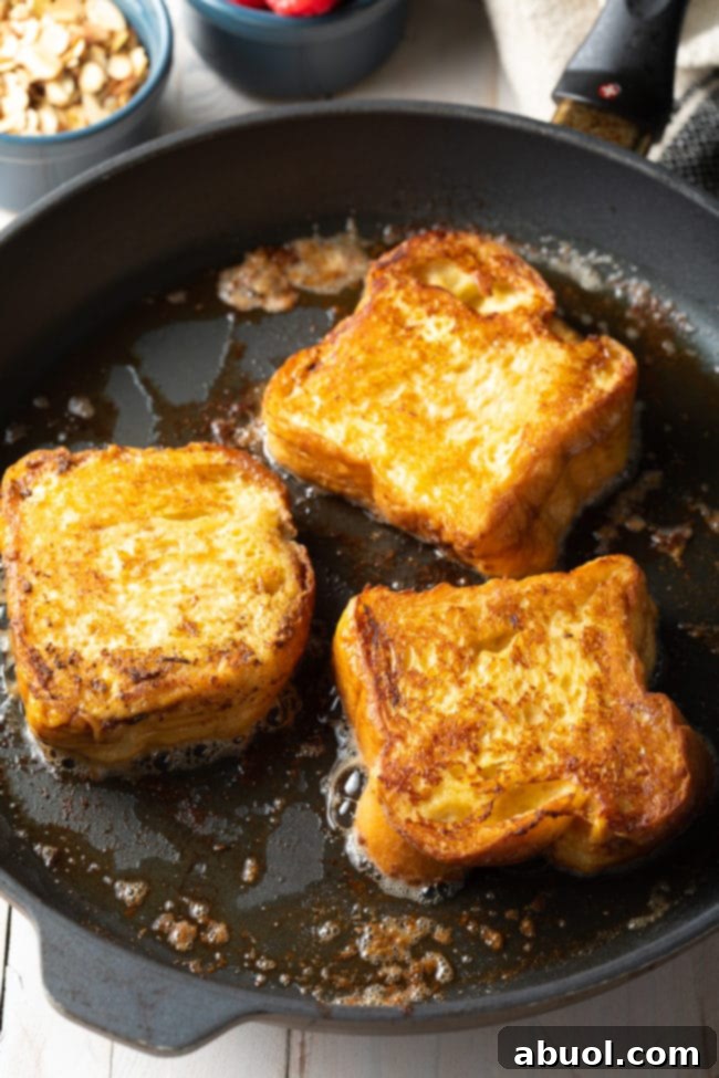 Three pieces of golden brown Pain Perdu sizzling in a hot skillet, edges crisping beautifully.