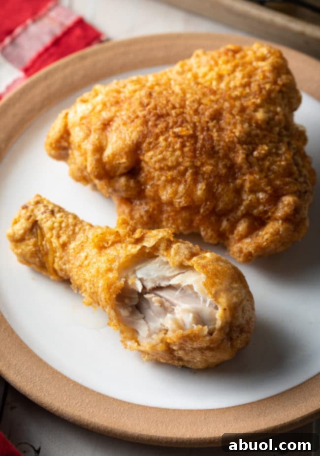 Top-down view of a breaded fried chicken thigh and drumstick on a white plate, with a bite taken from the drumstick, emphasizing the crispy texture and juicy meat.