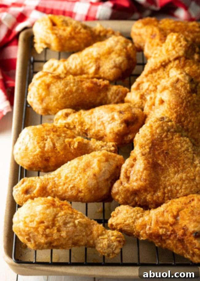 Several pieces of perfectly golden-brown fried chicken legs and thighs resting on a wire rack above a baking sheet to drain excess oil.
