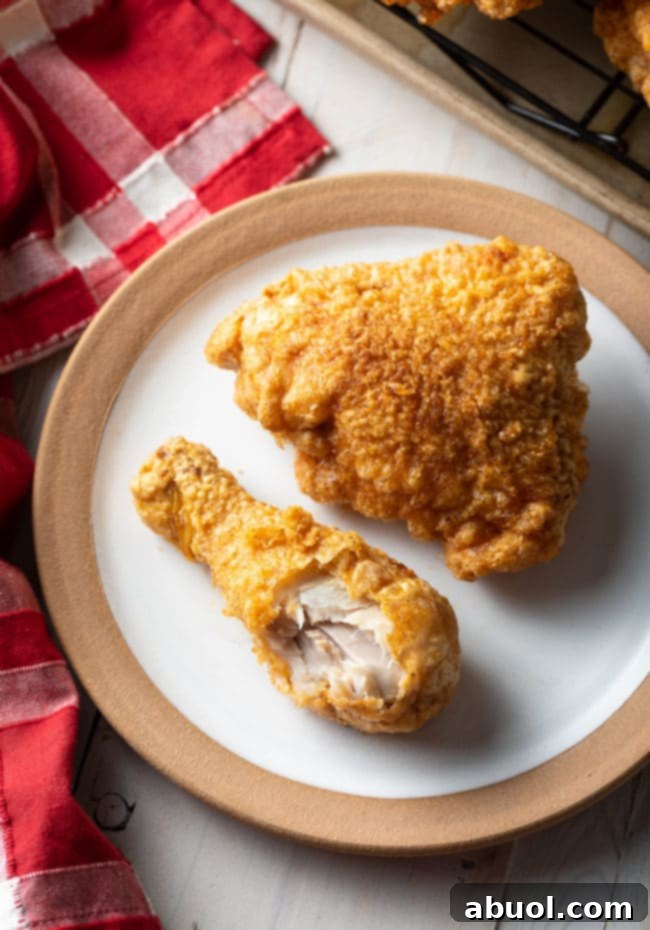 Top-down view of a golden-brown fried chicken thigh and drumstick on a white plate, with a bite taken from the drumstick to reveal the juicy interior.