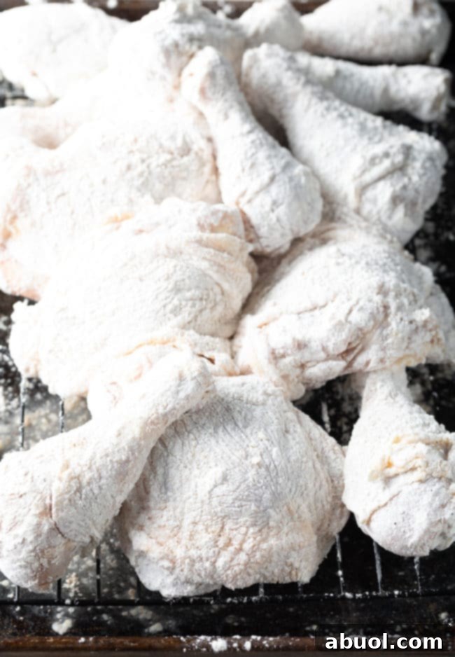 Several pieces of skin-on, bone-in chicken dredged in the seasoned flour and cornstarch mixture, resting on a wire rack.