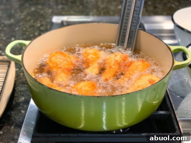 Chicken pieces frying in hot oil within a large green Dutch oven, turning golden brown and crispy.