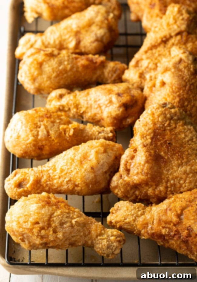 Several pieces of golden-brown fried chicken legs and thighs resting on a wire rack above a baking sheet to drain excess oil.