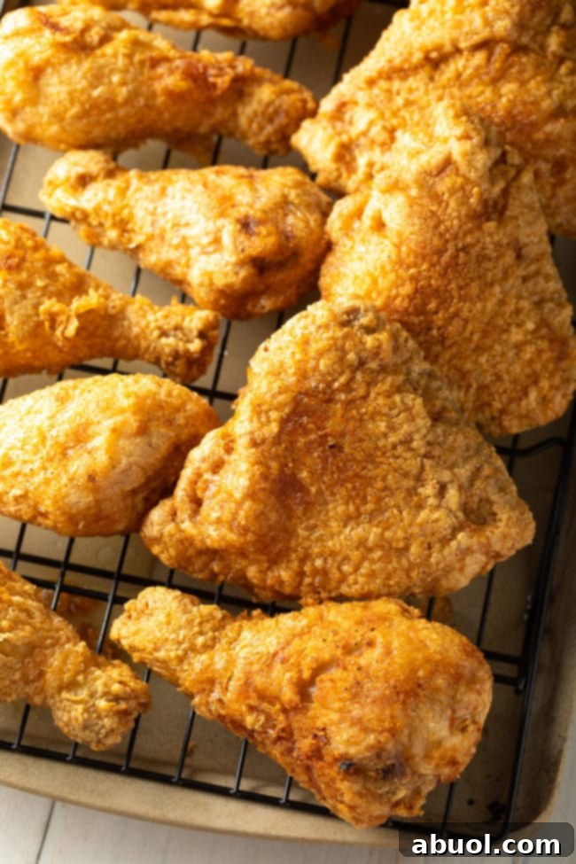 A generous serving of fried chicken legs and thighs arranged on a wire rack over a baking sheet, showcasing the crispy texture.
