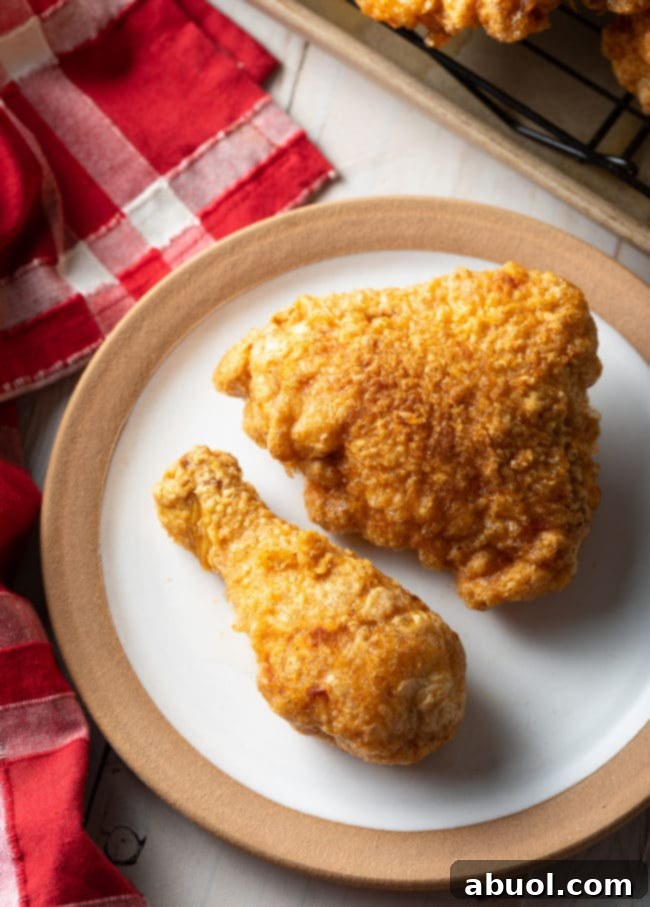 Top-down view of a golden-brown fried chicken thigh and drumstick on a white plate, showcasing the crispy texture.