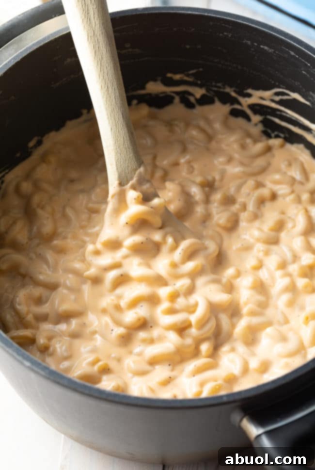 Homemade Mac and Cheese Perfection 4 Best Homemade Mac and Cheese - Top view of a wooden spoon stirring the stovetop pasta in cheese sauce