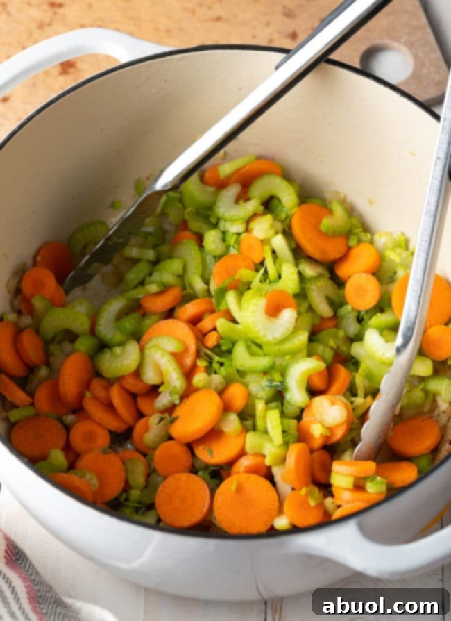 Vibrant carrots and crisp celery being sautéed in a large pot, releasing their natural sweetness.