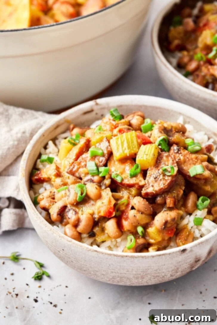 Closeup shot of hoppin john served over white rice in a bowl and garnished with fresh green onion. 