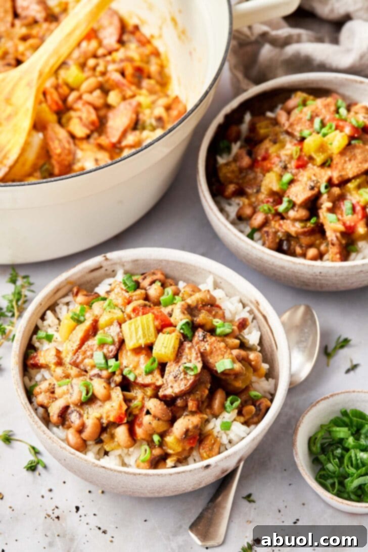 Closeup of hoppin john over rice served in a bowl with a small ramekin filled with fresh sliced green onion next to it. 