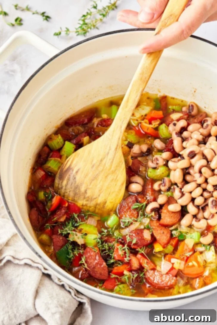 Overhead view of veggies, sausages and black eyes peas being cooked in pot. 