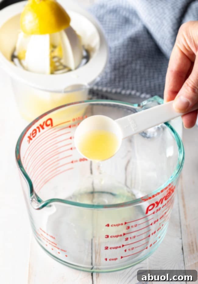 Glass measuring cup with a hand pouring lemon juice into it.