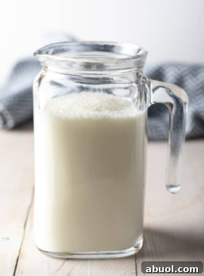 Side view of a small glass pitcher containing the finished homemade buttermilk.