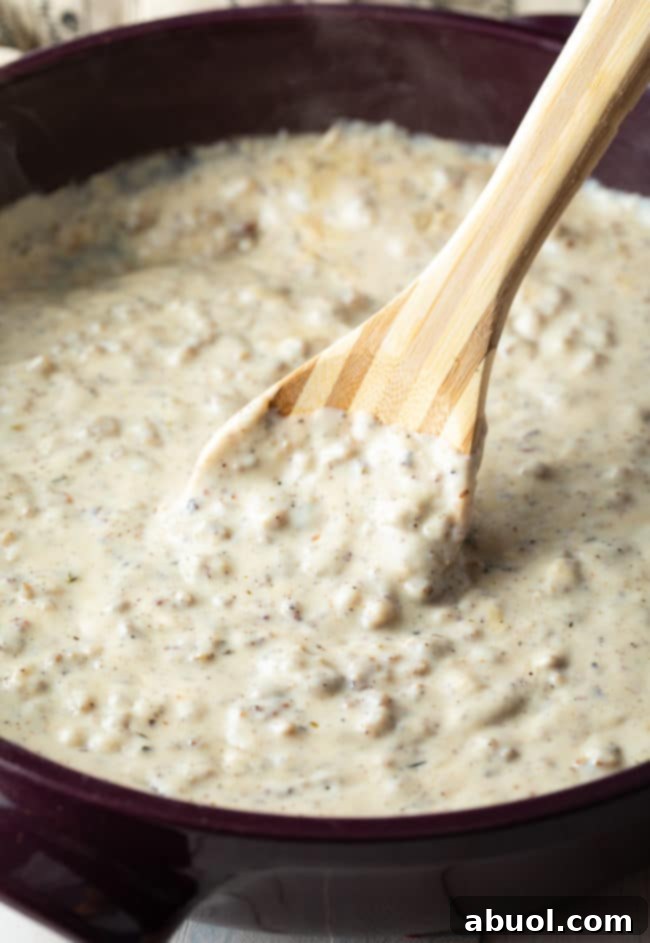 Effortless Sausage Gravy 2 Easy sausage gravy in a pan with a wooden spoon.