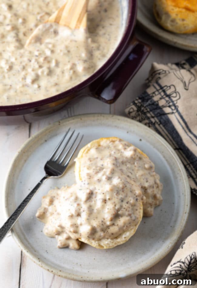 Effortless Sausage Gravy 3 Biscuit on a plate smothered in spicy sausage gravy with a fork.