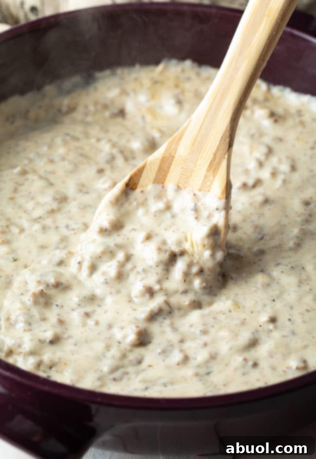 Effortless Sausage Gravy 5 Stirring Easy Sausage Gravy Recipe in a skillet with a wooden spoon.