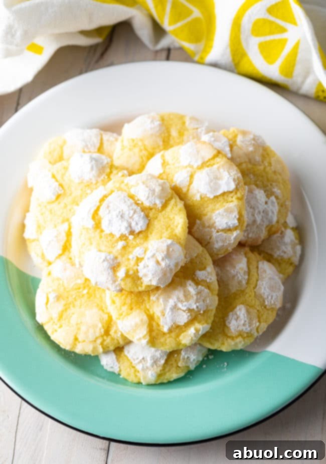 A beautifully arranged plate featuring a stack of golden lemon crinkle cookies dusted with powdered sugar, showcasing their perfect cracks and inviting texture.