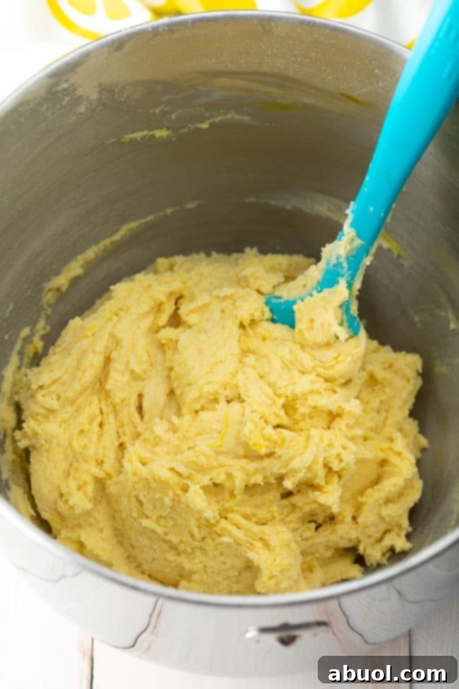A close-up shot of creamy, bright yellow lemon crinkle cookie dough being mixed in a bowl, showing its smooth texture.
