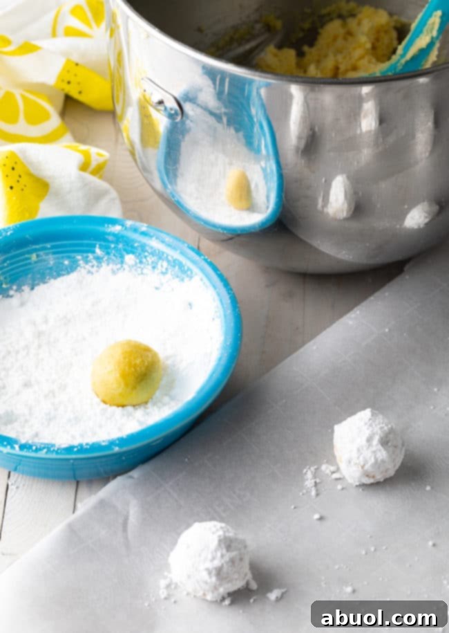 A perfectly rolled ball of lemon cookie dough being placed into a bowl filled with powdered sugar, ready for coating.