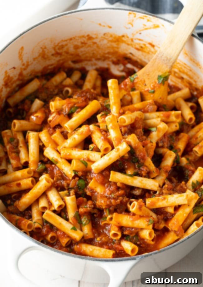 Italian-food Mixing ziti into meat sauce in a large pot, preparing for baking