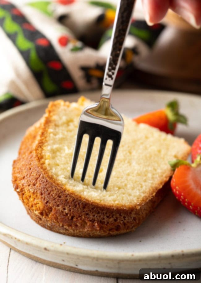 Close-up of a single slice of pound cake on a white dish with a fork, ready for a bite.