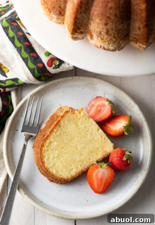 A single, perfectly sliced piece of cream cheese pound cake on a plate, garnished with fresh strawberries.